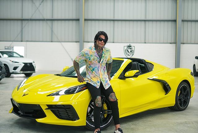 Yeferson Cossio posing in a colorful shirt on his yellow Chevrolet Corvette.